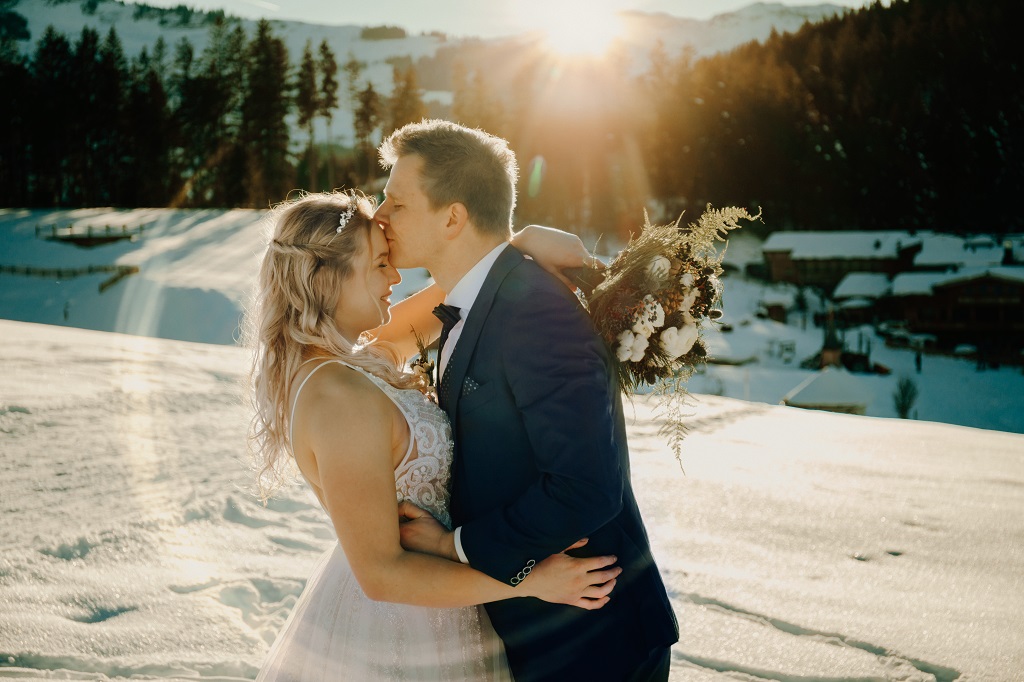 Brautpaar bei ihrer Winterhochzeit in den Bergen beim Shooting im Sonnenuntergang mit Brautstrauß