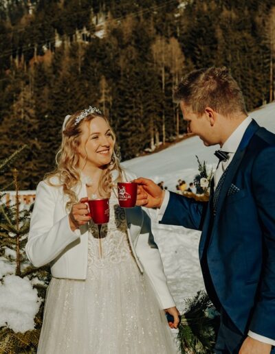 Brautpaar beim Anstoßen nach ihrer freien Trauung in den Bergen Österreichs im Winter