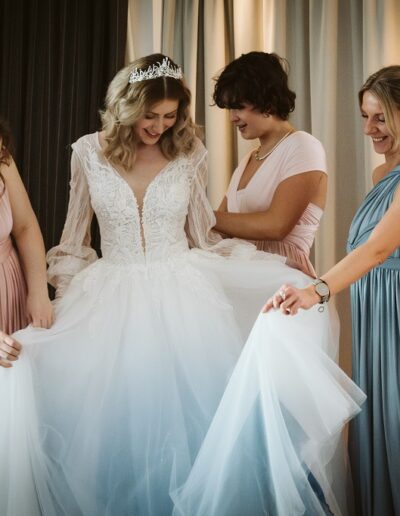 Brautjungfern helfen der Braut in ihr wunderschönes glitzerndes Brautkleid