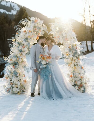 Brautpaar beim Shooting vor einem Traubogen im Schnee mit Felljacke