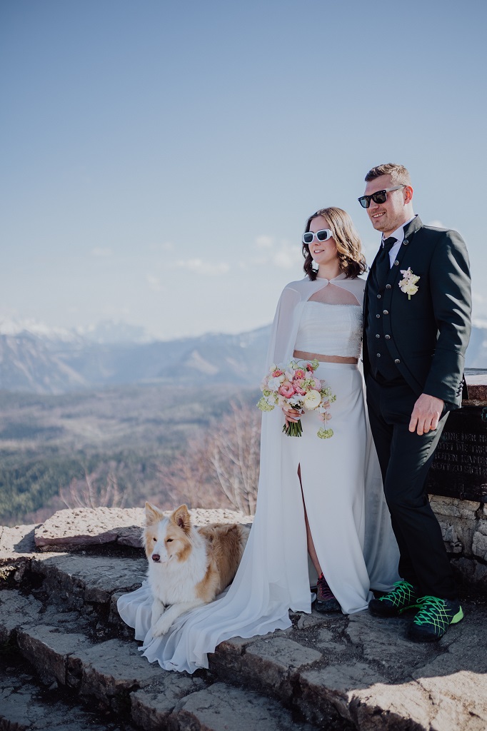 Ronja Weddings Hochzeitsplanerin Berghochzeit Locationscout südtirol Wörgl Tannheimer Tal Brautpaar mit ihrem Hund am Gipfelkreuz beim Fotoshooting auf ihrer Berghochzeit in Österreich
