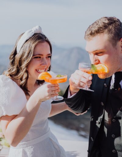 Glückliches Brautpaar auf ihrer Berghochzeit beim Anstoßen mit Aperol Spritz