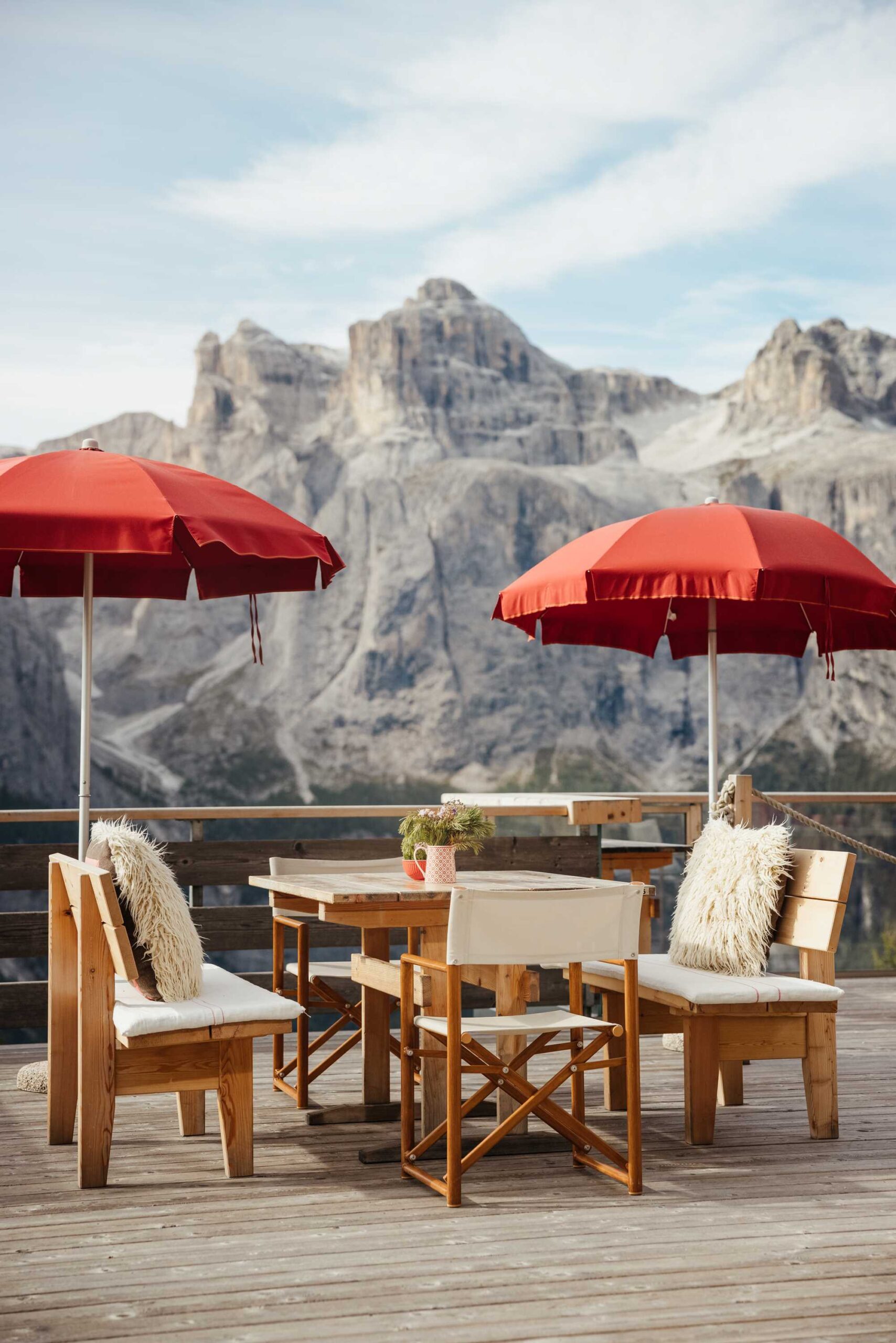 Gemütliche Sonnenterrasse einer Berghütte in den Dolomiten mit roten Sonnenschirmen und Fellkissen – traumhafte Location für eine intime Alpenhochzeit oder Winterhochzeit.