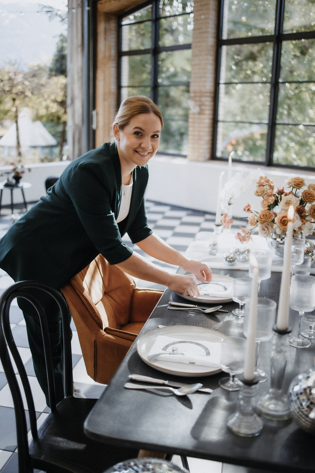 Eine lächelnde Frau, Ronja Baumbach, deckt einen Esstisch mit Kerzen und Blumen in einem hellen, modernen Raum, der eine perfekte Atmosphäre für eine standesamtliche Trauung oder eine intime Berghochzeit in Österreich schafft.