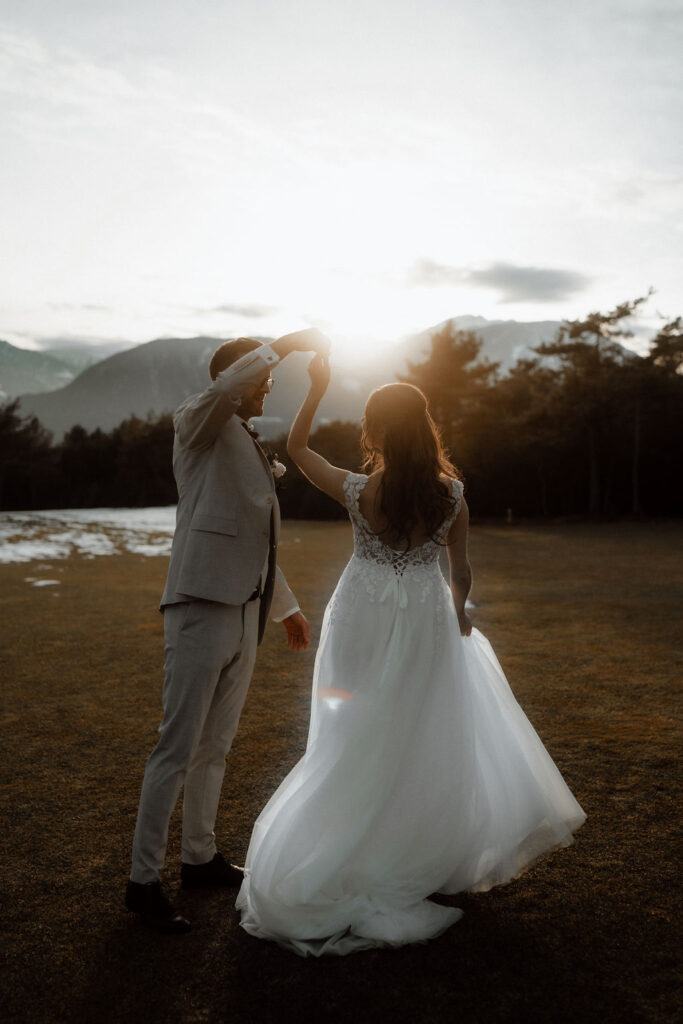 Braut und Bräutigam tanzen im Freien bei Sonnenuntergang, mit Bergen und Bäumen im Hintergrund, und feiern ihre kleine Winterhochzeit in Österreich.