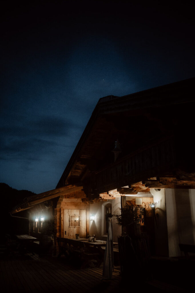 A rustic cabin with glowing lights is visible at night under a dark, cloudy sky, an enchanting wedding venue in Austria, perfect for a civil ceremony.