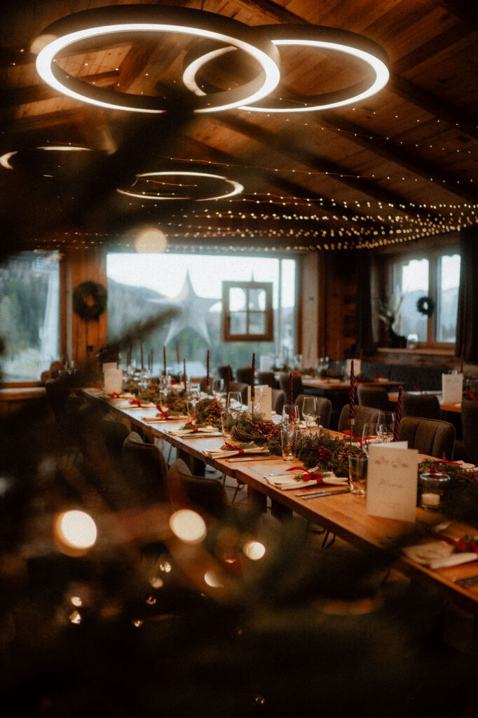 Ein rustikaler Speisesaal in Österreich mit langen Tischen für ein festliches Essen, perfekt für eine Berghochzeit oder standesamtliche Trauung, schön dekoriert mit Kerzen und Grünzeug.