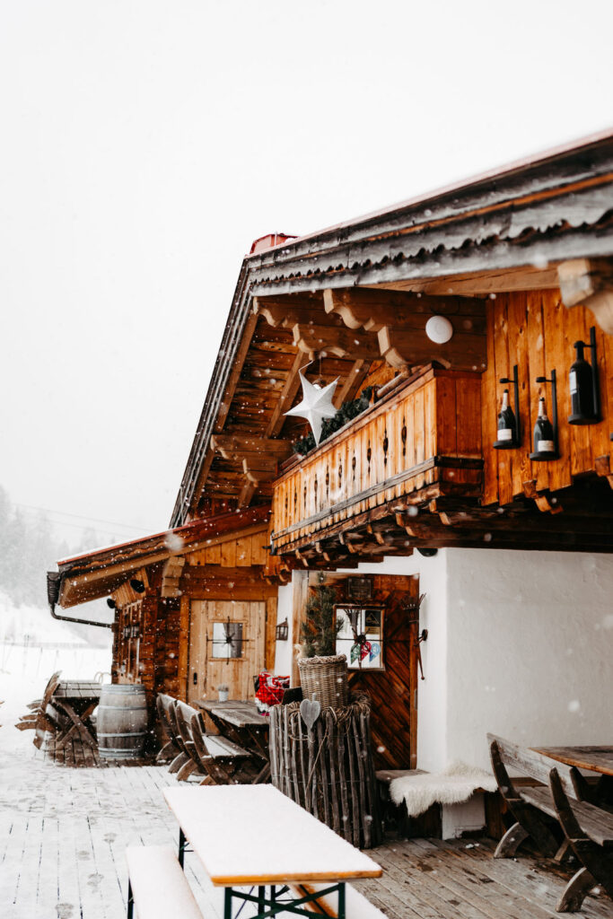 Ein rustikales Holzchalet in Tirol, Österreich, mit einer verschneiten Terrasse, Bänken und einer bezaubernden verschneiten Umgebung - perfekt für eine zauberhafte Berghochzeit.