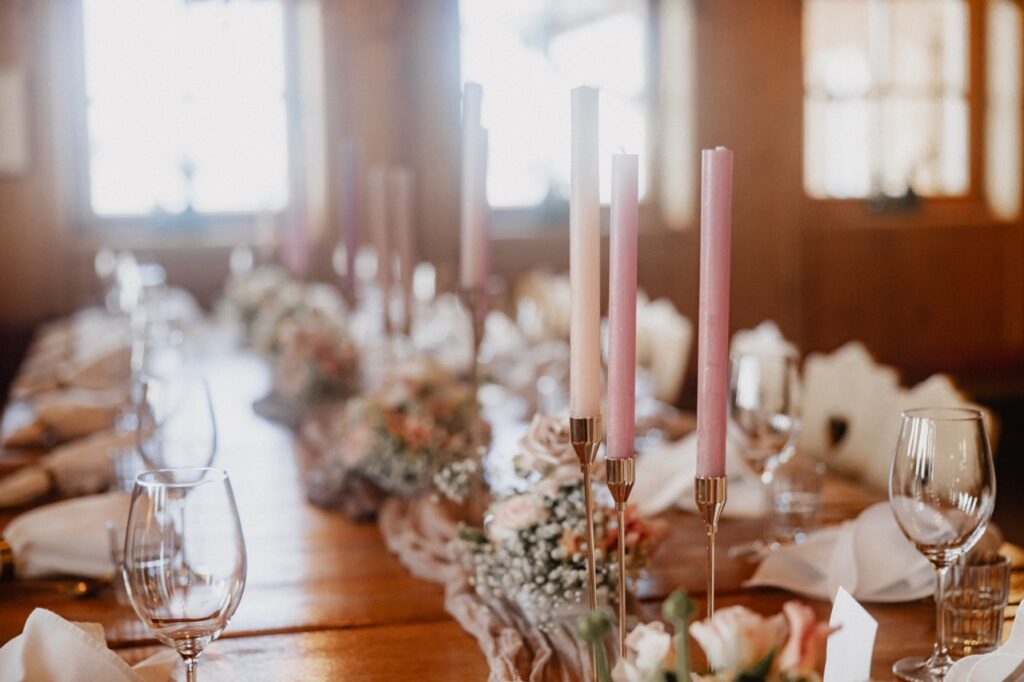 Elegant gedeckter Tisch mit rosa Kerzen, Gläsern und floralen Tafelaufsätzen in einem warm beleuchteten Raum - perfekt für eine Berghochzeit in Tirol oder als Ihre Traum-Hochzeitslocation.