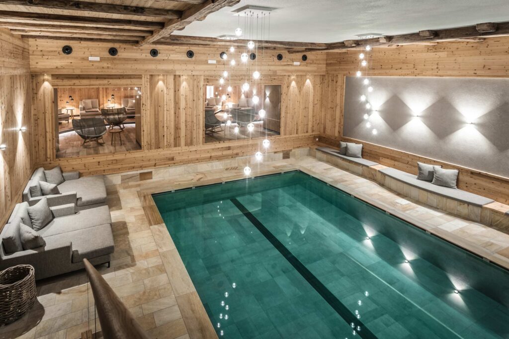 Innenpool mit klarem Wasser, grauen Sitzgelegenheiten, Holzwänden und Hängelampen in einem gemütlichen, modernen Raum.