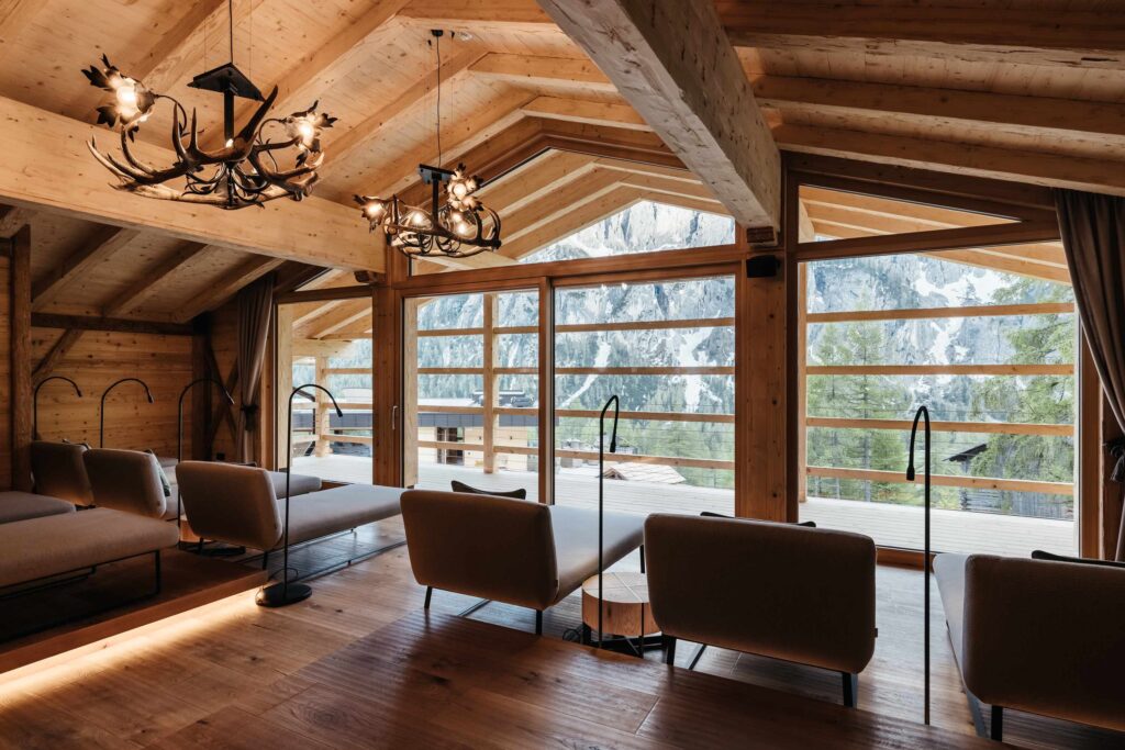 Gemütlicher Aufenthaltsraum aus Holz mit modernen Sofas, großen Fenstern und Blick auf die Berge.