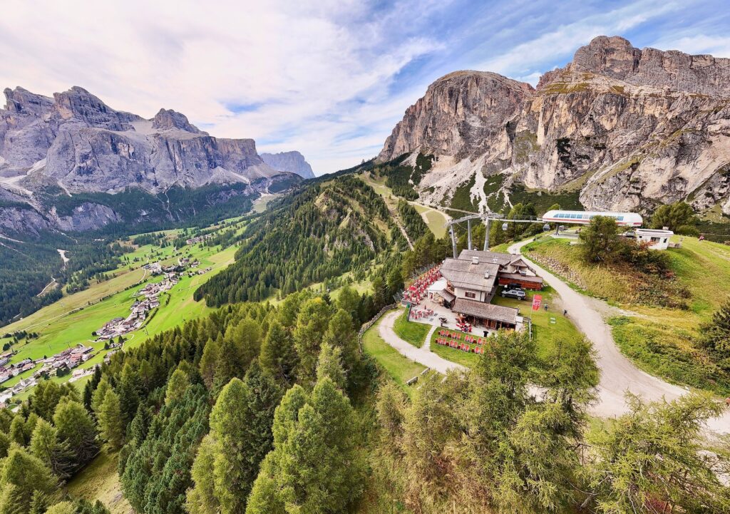 Bergdorf mit grünem Tal, Wald, felsigen Gipfeln und einer Hütte mit Sitzgelegenheiten im Freien, umgeben von malerischen Aussichten.